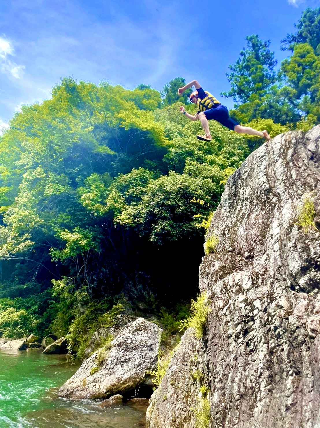 空に向かってジャンプする川遊びの一場面