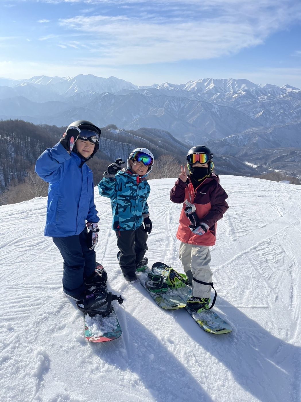青空の雪山でスノーボードを楽しむ子どもたち
